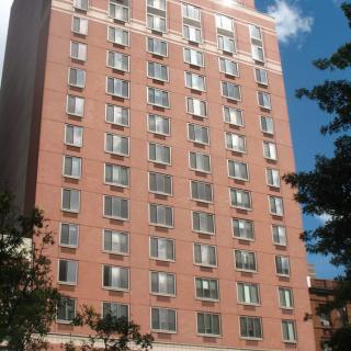 A tall brick building with numerous windows against a blue sky, framed by trees.