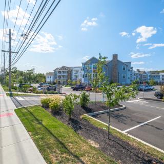 A modern apartment complex with a large parking lot and landscaped surroundings on a sunny day.