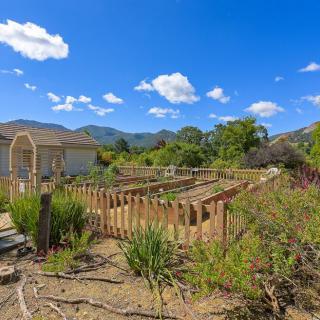 A tranquil garden surrounded by a wooden fence, set against a backdrop of mountains and a clear blue sky.