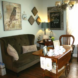 A cozy vintage-inspired living room with a dark green sofa, artwork of a bird on the wall, and a small table set up for tea.