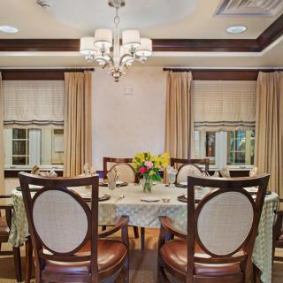 A luxurious dining room featuring an elegant table setting with a chandelier above and decorative curtains framing the windows.