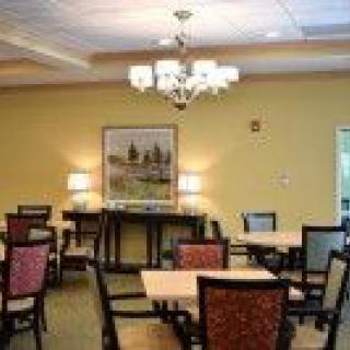 A cozy dining room with neatly arranged tables and chairs, featuring a chandelier and decorative painting on the wall.