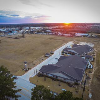 An aerial view of a suburban residential area at sunset, with houses lining the road and an open field nearby.