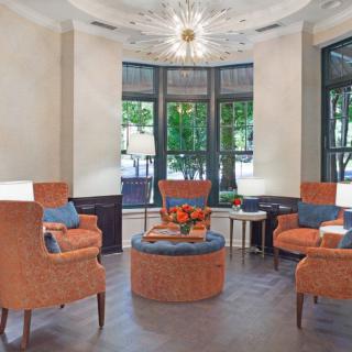 A cozy seating area in a lobby with armchairs, a central ottoman, and large windows.