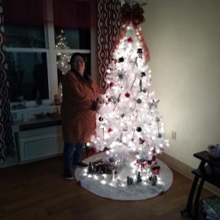 A woman decorating a beautifully lit Christmas tree at home.