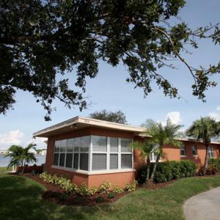 A brick house with large windows surrounded by palm trees and a well-maintained lawn.