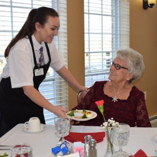 A waitress serves a meal to an elderly woman in a restaurant setting.