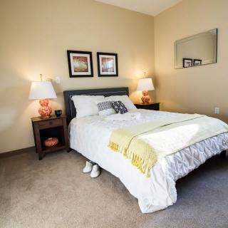A cozy bedroom with a neatly made bed, two lamps on nightstands, and framed pictures on the wall.