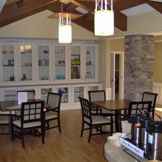 A cozy dining area with wooden floors, tables, and chairs, featuring elegant lighting and a stone column.