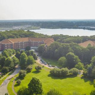 Aerial view of a building surrounded by lush greenery and a nearby lake.