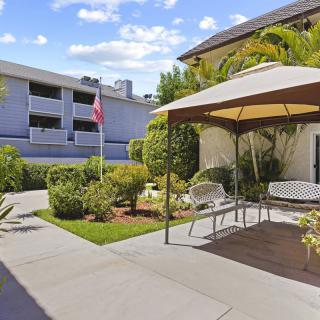 A peaceful courtyard featuring a gazebo with benches, surrounded by lush greenery and adjacent to an apartment building on a sunny day.
