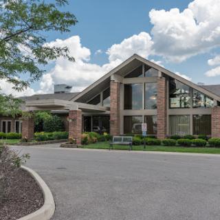 A modern architectural building featuring large windows and a welcoming entrance, set against a backdrop of blue sky and fluffy clouds.