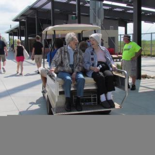 A group of people sit on a golf cart, enjoying a sunny day outdoors.