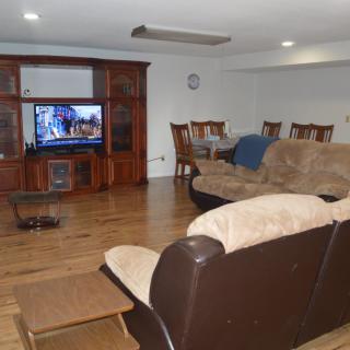 A spacious living room featuring a comfortable sofa, a TV set in a wooden entertainment center, and a dining area with a table and chairs.