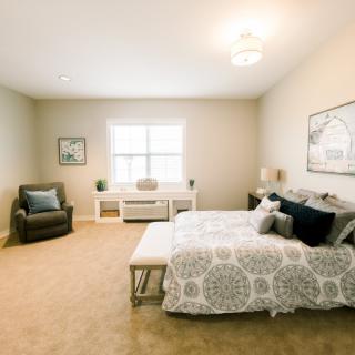 A cozy and spacious bedroom with modern decor, featuring a bed, armchair, and simple artwork.