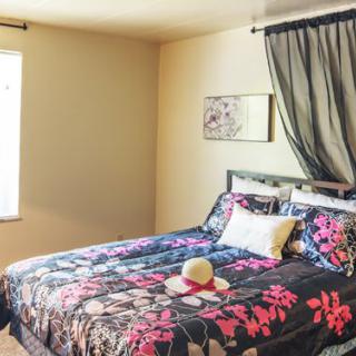 A cozy bedroom with floral bedding and sheer curtains.