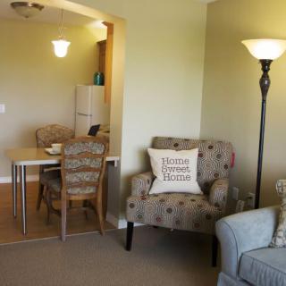 A cozy living room with an armchair and a floor lamp, adjacent to a dining area.
