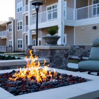 A cozy outdoor area with a fire pit and seating in front of a modern apartment building.