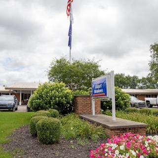 A welcoming view of a facility with an American flag and colorful flowers in the foreground.