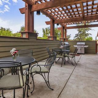 A spacious outdoor patio with a pergola, featuring tables and chairs, adorned with flowers, and a grill in the background.