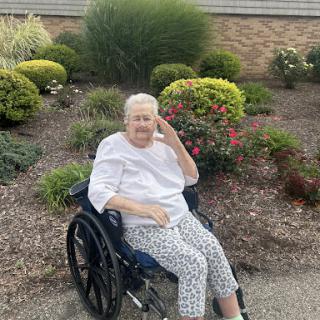 An elderly woman enjoying a sunny day in the garden, seated comfortably in her wheelchair.