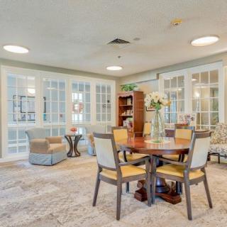 A cozy living room featuring a round table with chairs, surrounded by a carpeted floor and bookshelves.