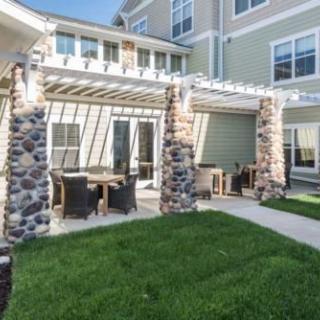 A modern patio with a pergola and outdoor furniture, complemented by stone columns and surrounded by a lush green lawn.