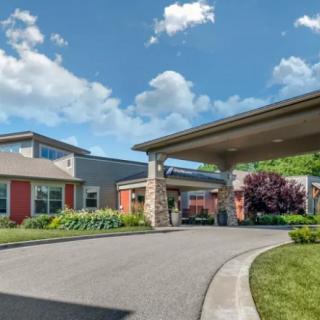 A modern building featuring a covered entrance and landscaped driveway under a clear blue sky.