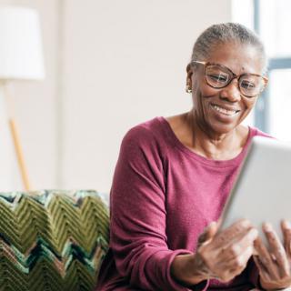 A senior woman smiling while using a tablet indoors.