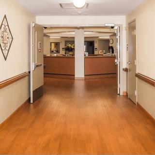 A well-lit hallway leading to a nursing station with wooden flooring and open doors.