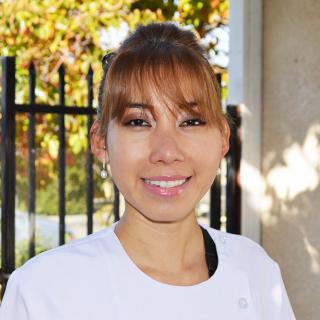 A woman smiling outdoors with an autumn background.
