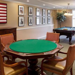 A cozy game room featuring a green poker table and pool table, adorned with framed wall art and comfortable chairs.