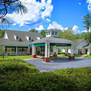 A picturesque building with a covered entrance surrounded by greenery and a blue sky with clouds.