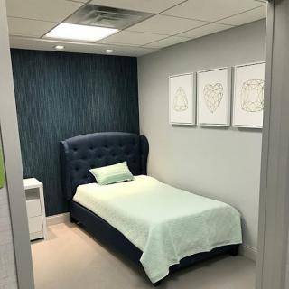 A minimalist bedroom featuring a single bed with a blue headboard and mint green bedding, complemented by modern artwork on the walls.
