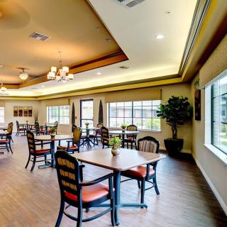 A spacious dining area with neatly arranged tables and chairs, large windows allowing natural light, and elegant lighting fixtures.