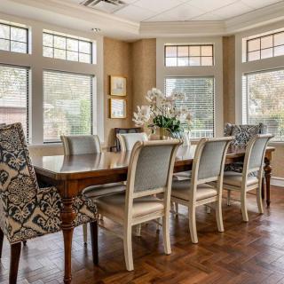 A beautifully lit dining room featuring an elegant wooden table surrounded by upholstered chairs, with large windows allowing natural light to fill the space.