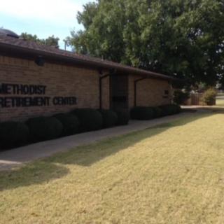A brick building housing a Methodist retirement center surrounded by grass and trees.