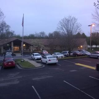 A view of a building with a parking lot during the evening, featuring several cars and trees.