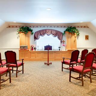 Interior view of a small auditorium with red chairs arranged in rows facing a stage.