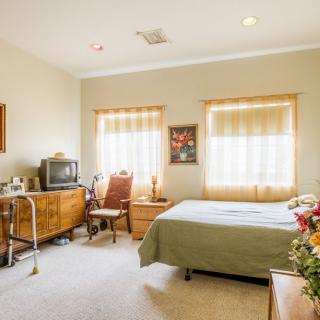 A cozy bedroom with a bed, vintage TV, dresser, and large windows letting in natural light.
