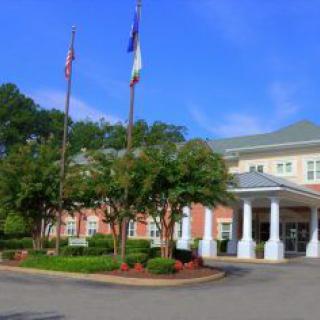 A building with flags and a landscaped entrance featuring columns.