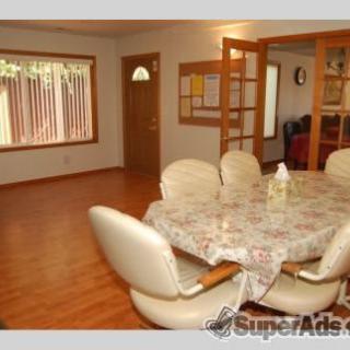 A spacious dining room with a round table, chairs, and wooden flooring.