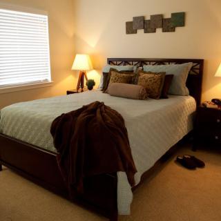 A cozy bedroom with a neatly made bed, soft lighting from lamps, and decorative pillows.