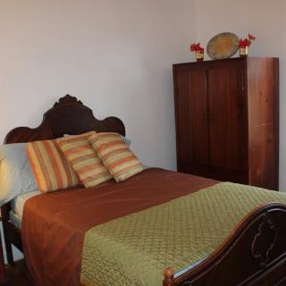 A cozy bedroom with a wooden bed and wardrobe, adorned with striped pillows and a decorative quilt.