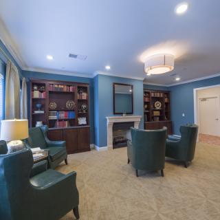 A cozy living room with blue walls, featuring bookshelves, armchairs, and a fireplace.