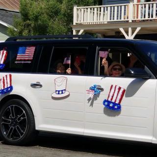 A car decorated with American flags and patriotic symbols participates in a parade.