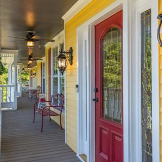 A charming porch with a red door and yellow exterior features outdoor seating and elegant lantern lights.