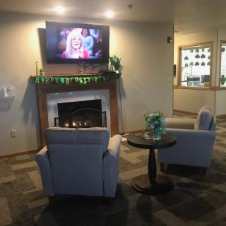 A cozy lobby with a fireplace, two chairs, and a television.