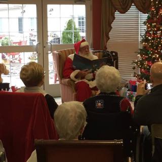 Santa Claus reading to an attentive audience during a festive holiday gathering.