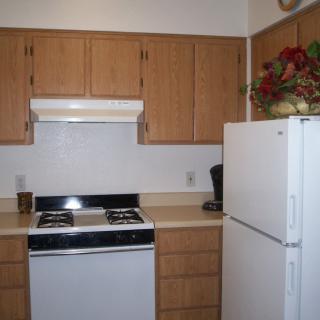 A compact kitchen featuring a refrigerator, stove, and wooden cabinets.